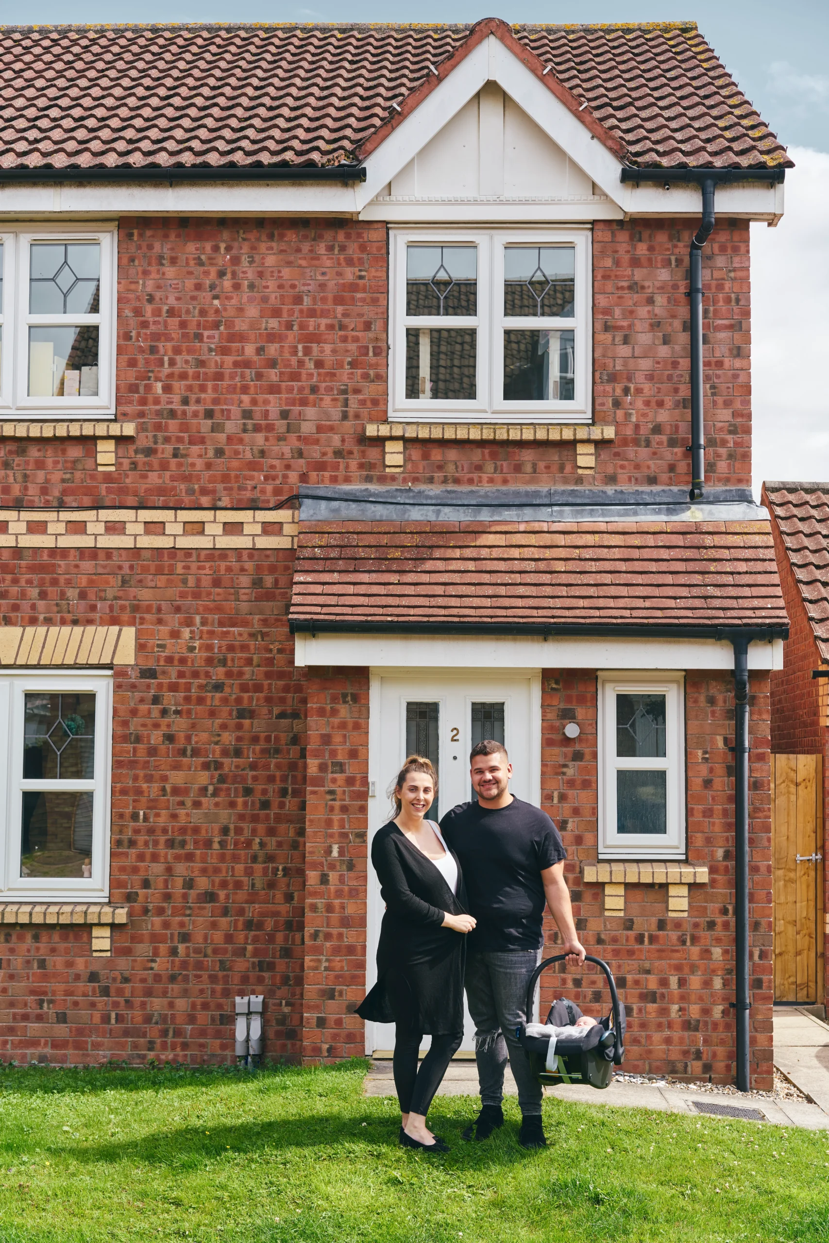 Smiling couple standing proudly in front of their new brick home.